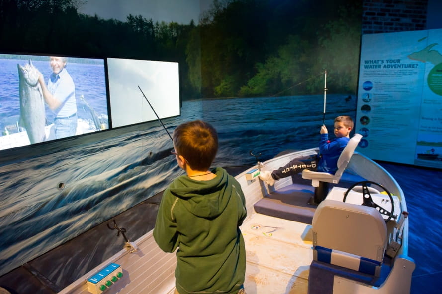 boys try out fishing simulator at Outdoor Adventure Center, with monitor showing fishing scenes