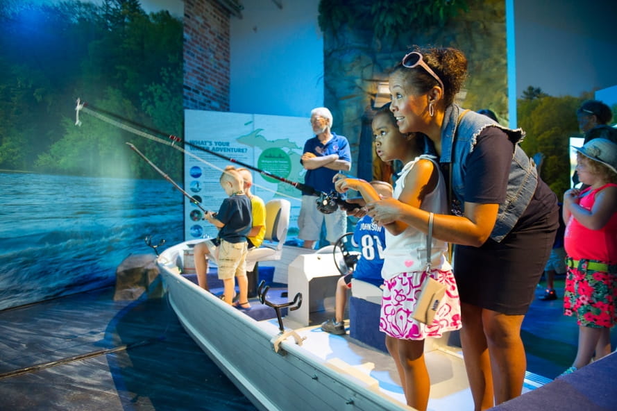 mom helps young girl try out fishing simulator at Outdoor Adventure Center