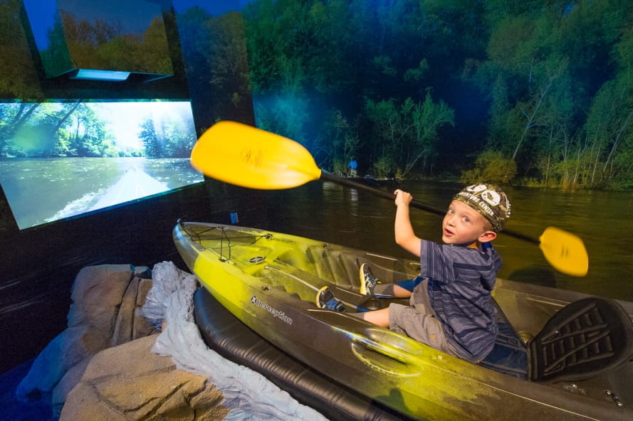 young boy, holding paddle, tries out kayaking simulator at Outdoor Adventure Center