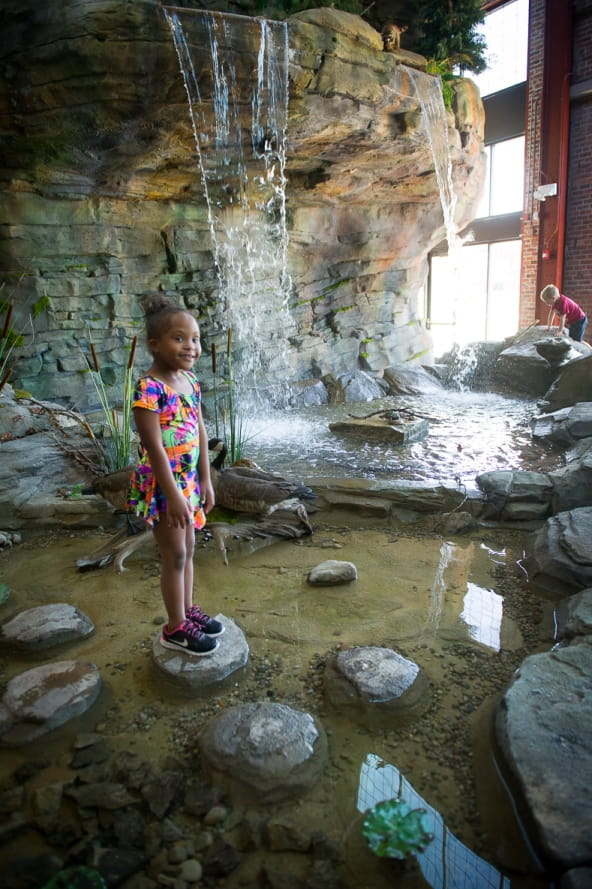 young girl stands on rock in front of Outdoor Adventure Center waterfall
