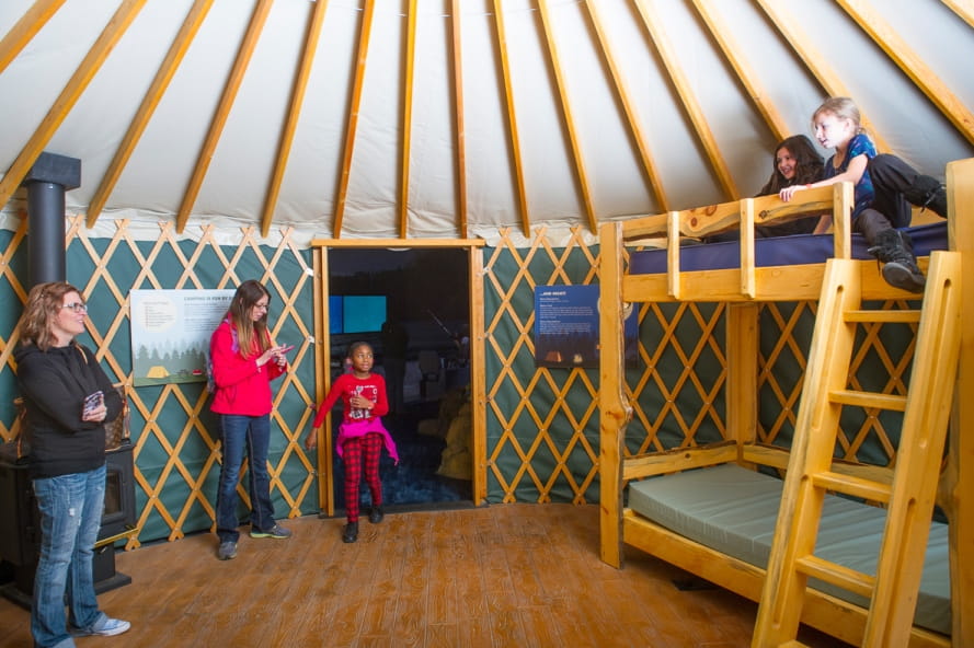 Visitors inside of the yurt replica at the Outdoor Adventure Center, girls on top of bunkbed