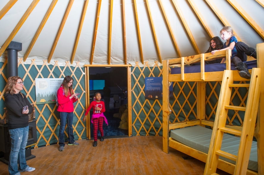 Visitors inside of the yurt replica at the Outdoor Adventure Center, girls on top of bunkbed