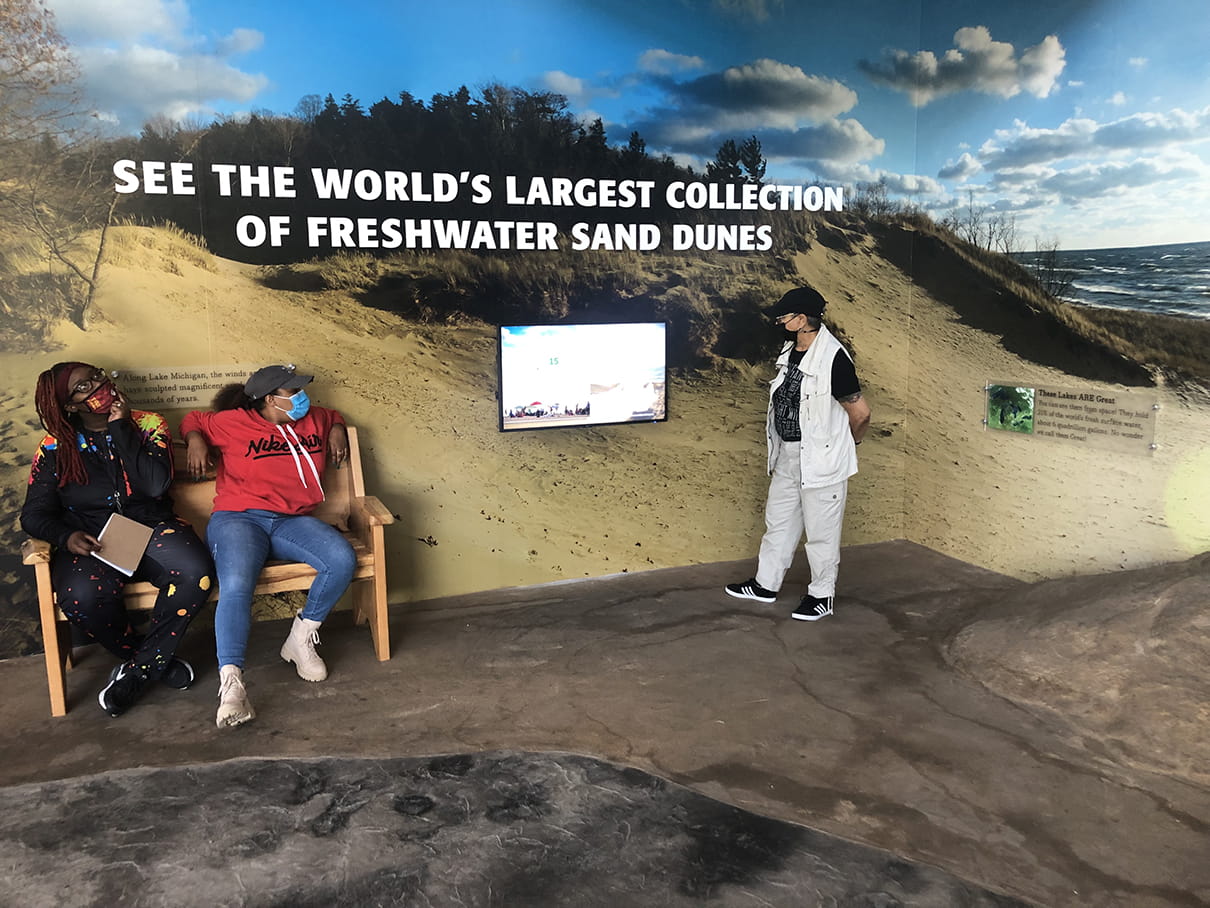 Visitors sitting on bench and looking at video screen in sand dune exhibit