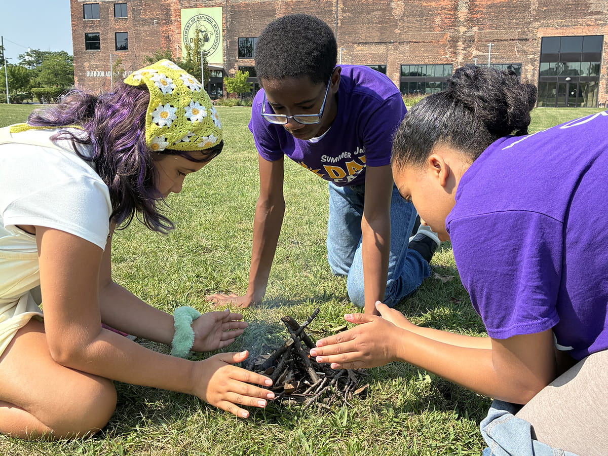 three summer camp attendees build small campfire