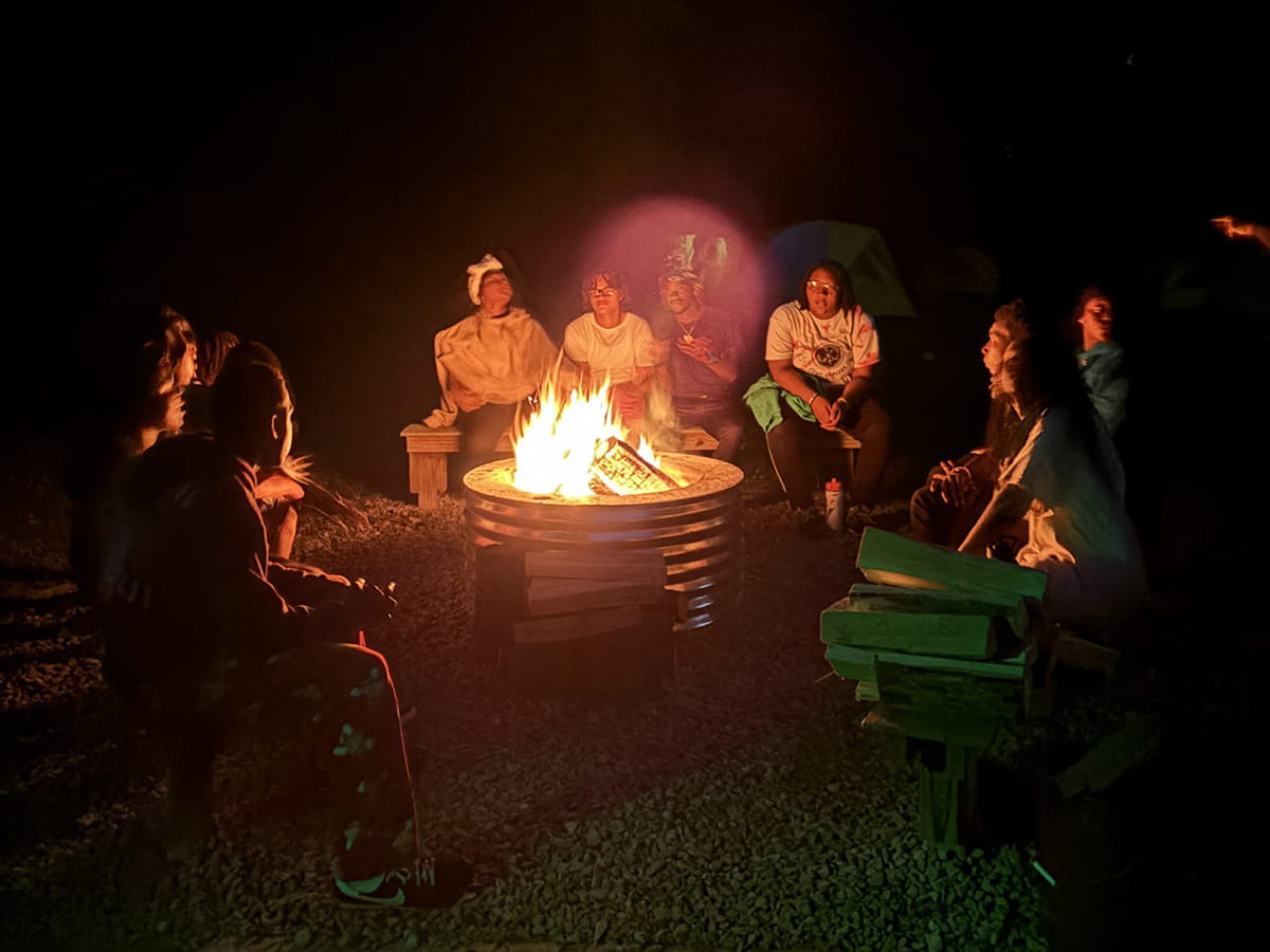 group of teenagers around a campfire pit at night