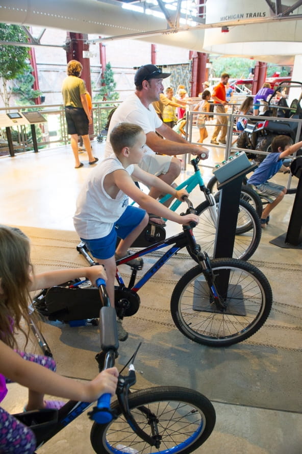 man and kids ride mountain biking simulators at the Outdoor Adventure Center