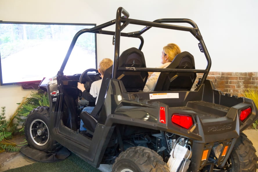 boy and woman ride in off-road vehicle simulator at the Outdoor Adventure Center