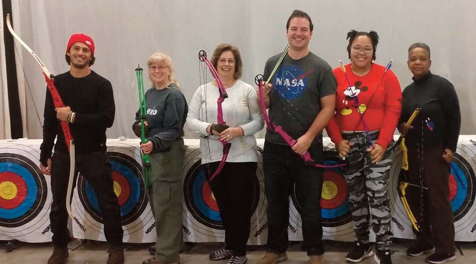 group of people holding bows and arrows in front of archery targets
