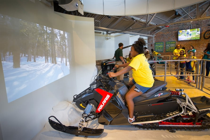girl rides snowmobile simulator at the Outdoor Adventure Center