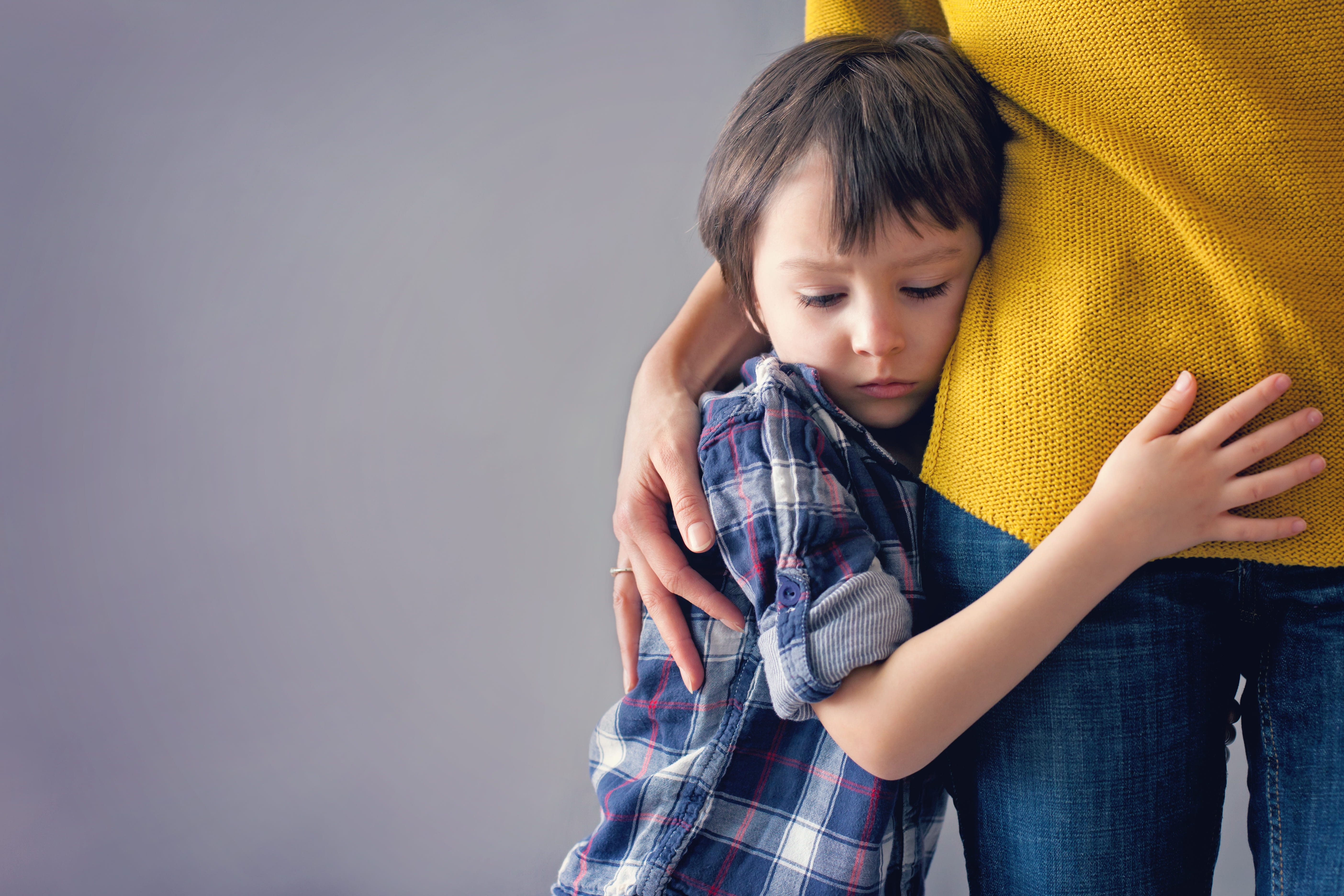 sad child hugging the hip of an adult