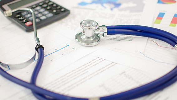 Stethoscope next to a calculator on top of budget sheets spread out on a desk