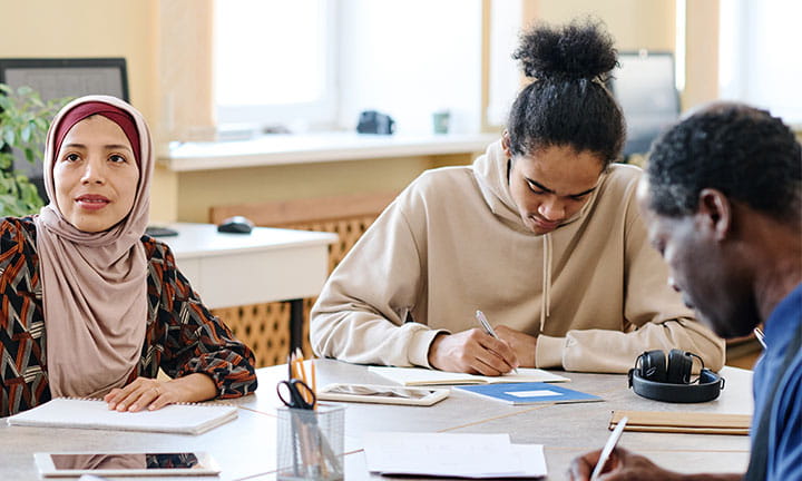 three people sitting at a table in a language learner class working and asking questions