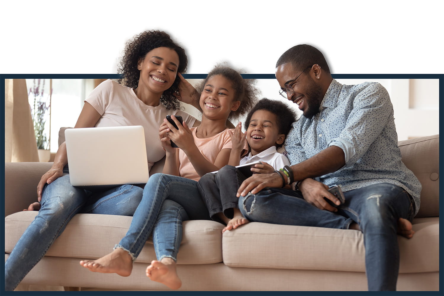 black family laughing on the couch wih phone and laptop