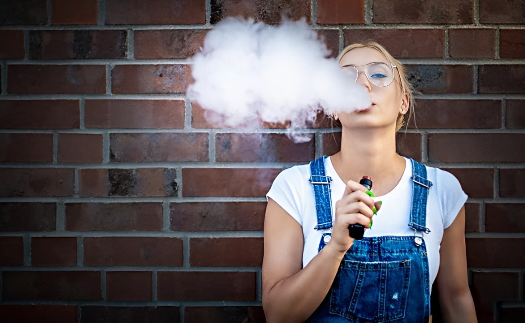 Young Girl blowing out large pillow of vaping mist next to a red brick building
