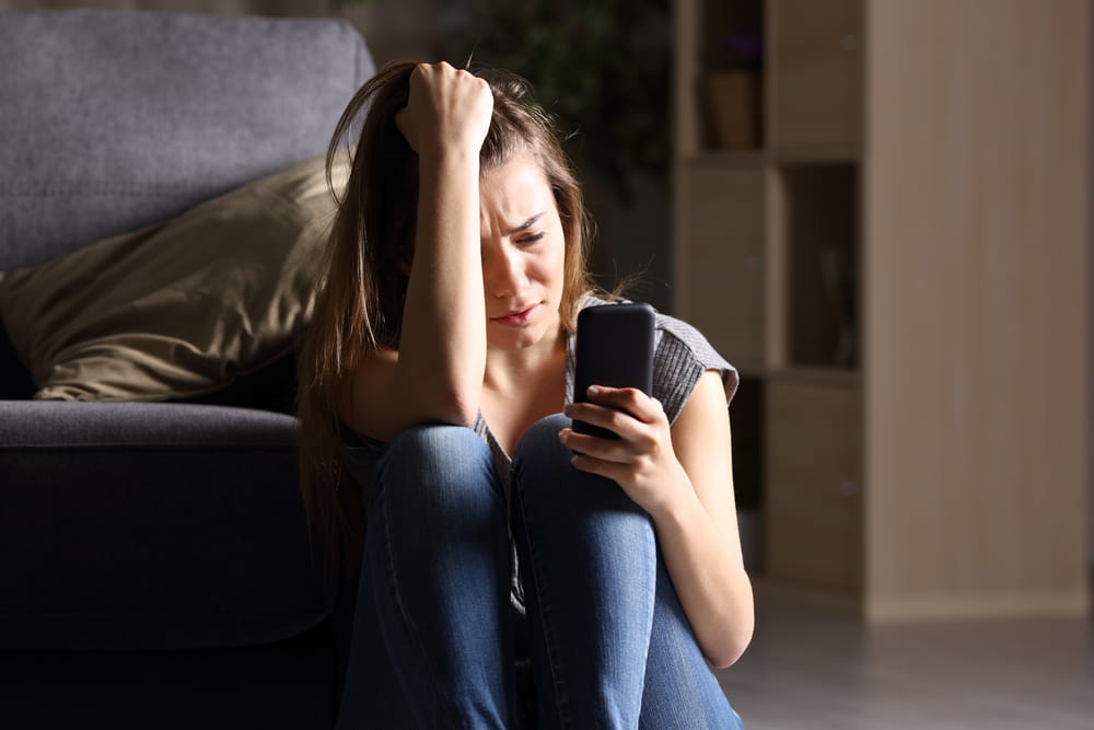 woman sitting down looking at her phone; sadly