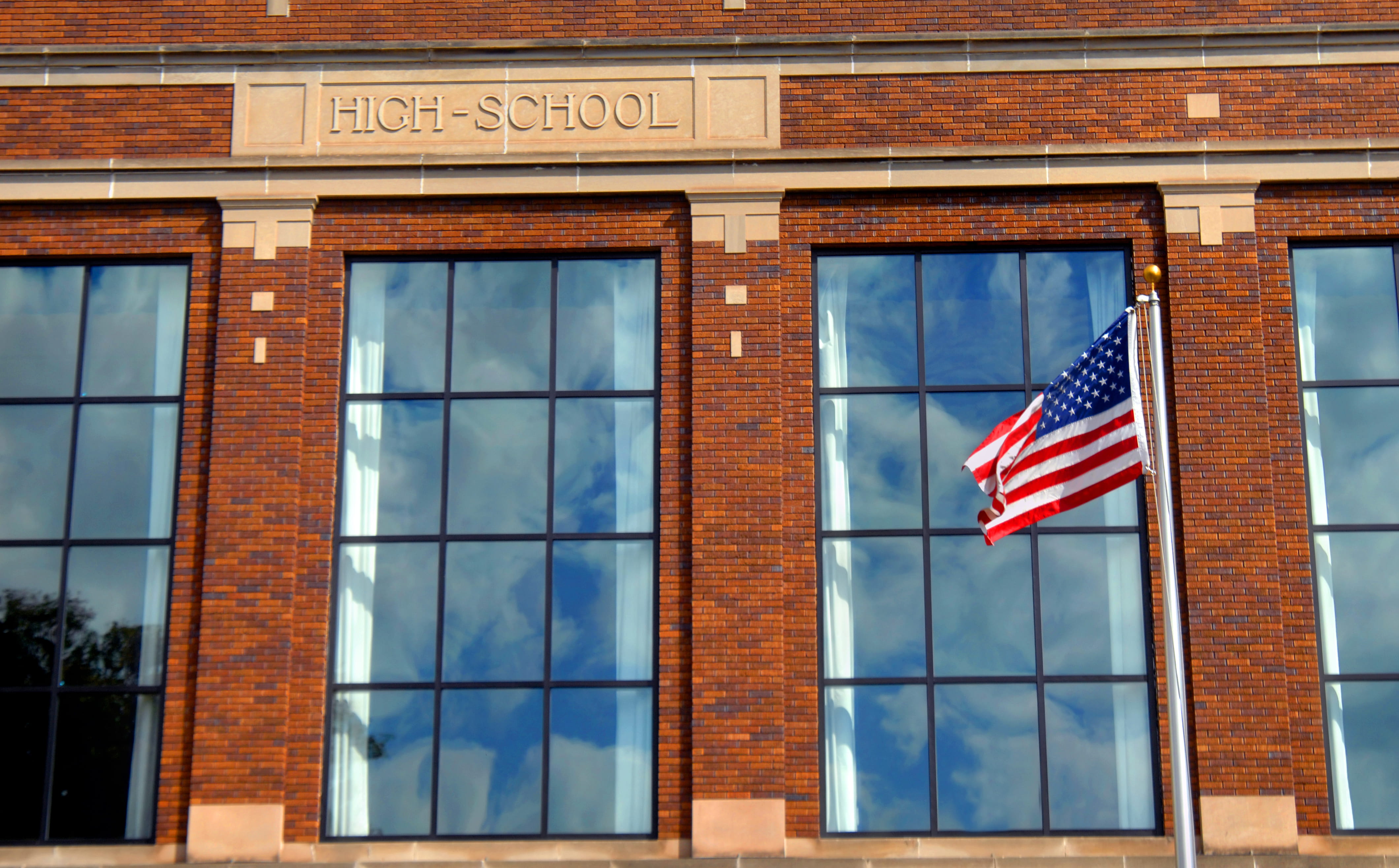 Brick front high school with large grid windows and American flag flying. 