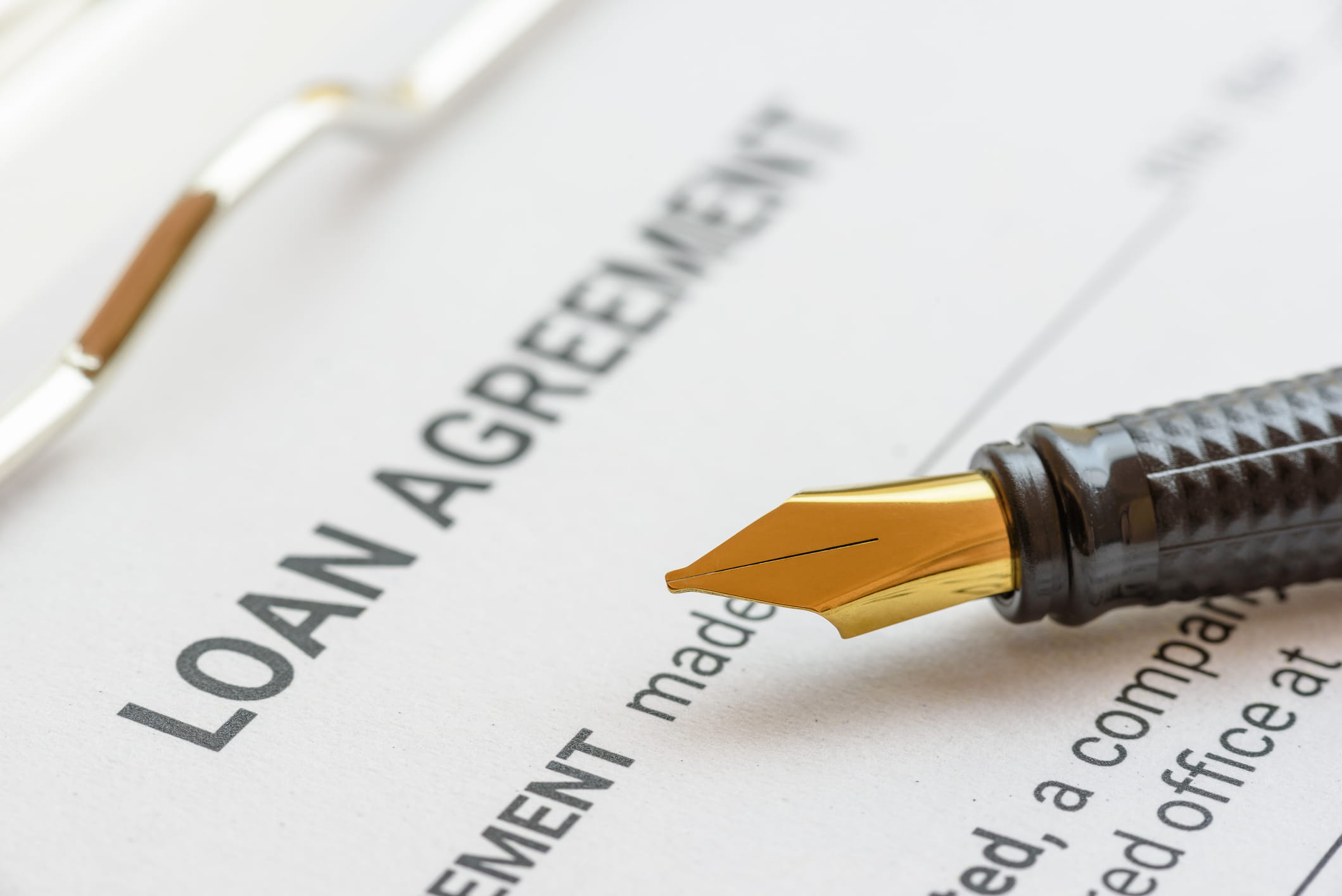 Close-up of a "LOAN AGREEMENT" document on a clipboard. A black fountain pen with a gold nib rests on the paper, positioned just below the header.