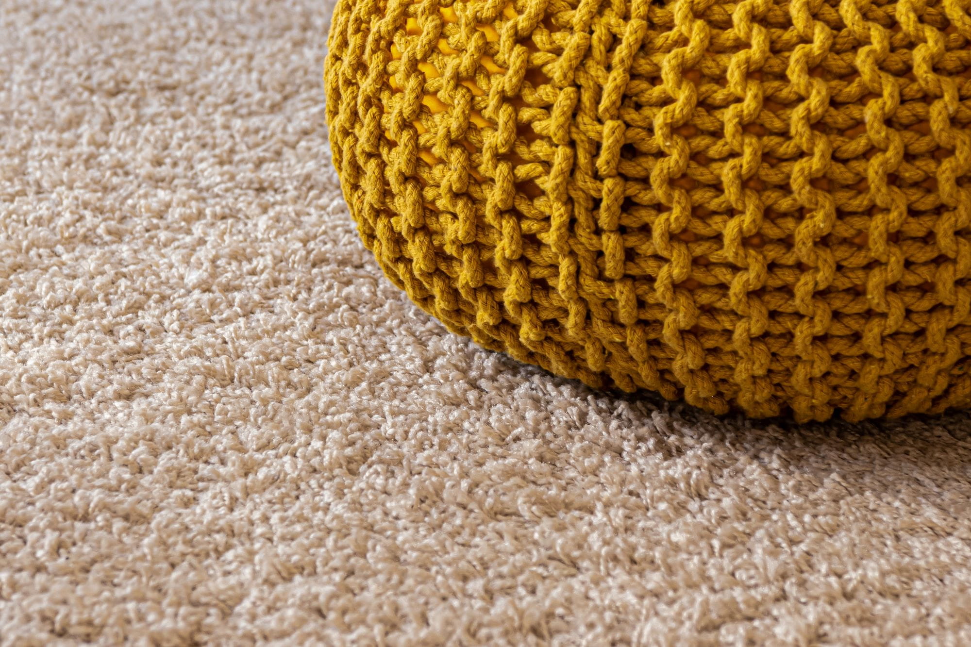 A yellow cushion on a beige carpet