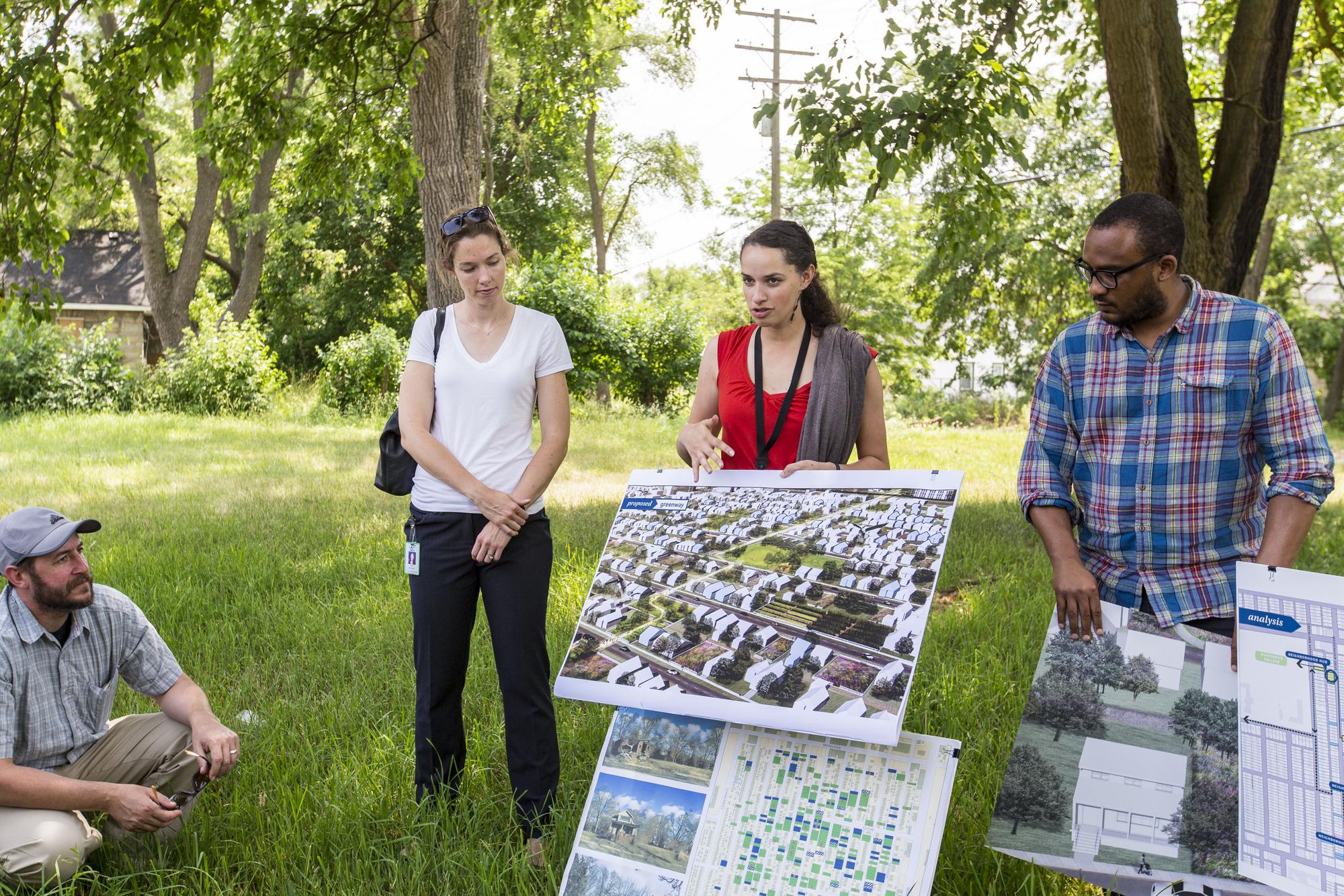Three community members with posters at a park, presenting information to other community members