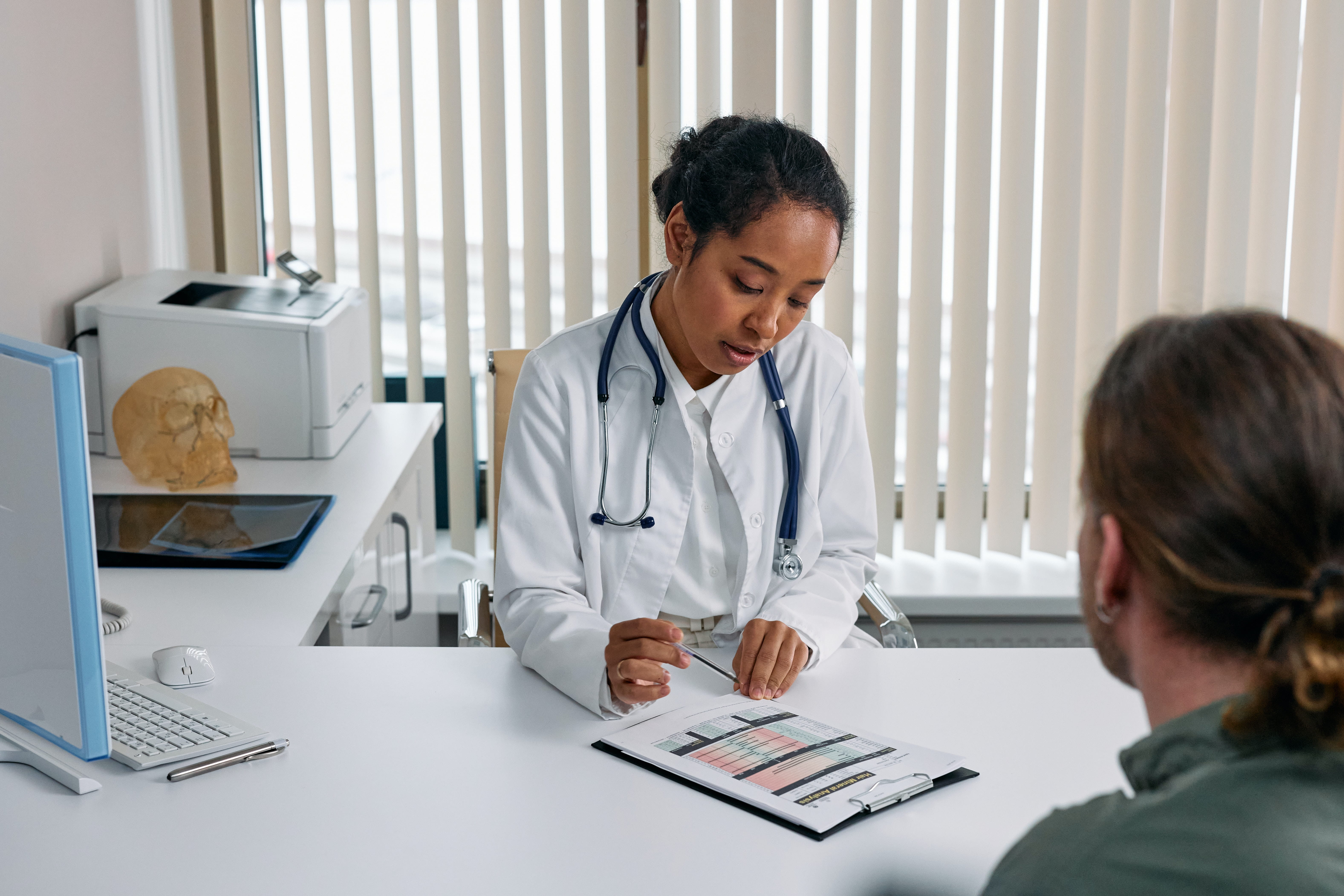 A female doctor siting at a desk in an office, going over a medical chart with a patient