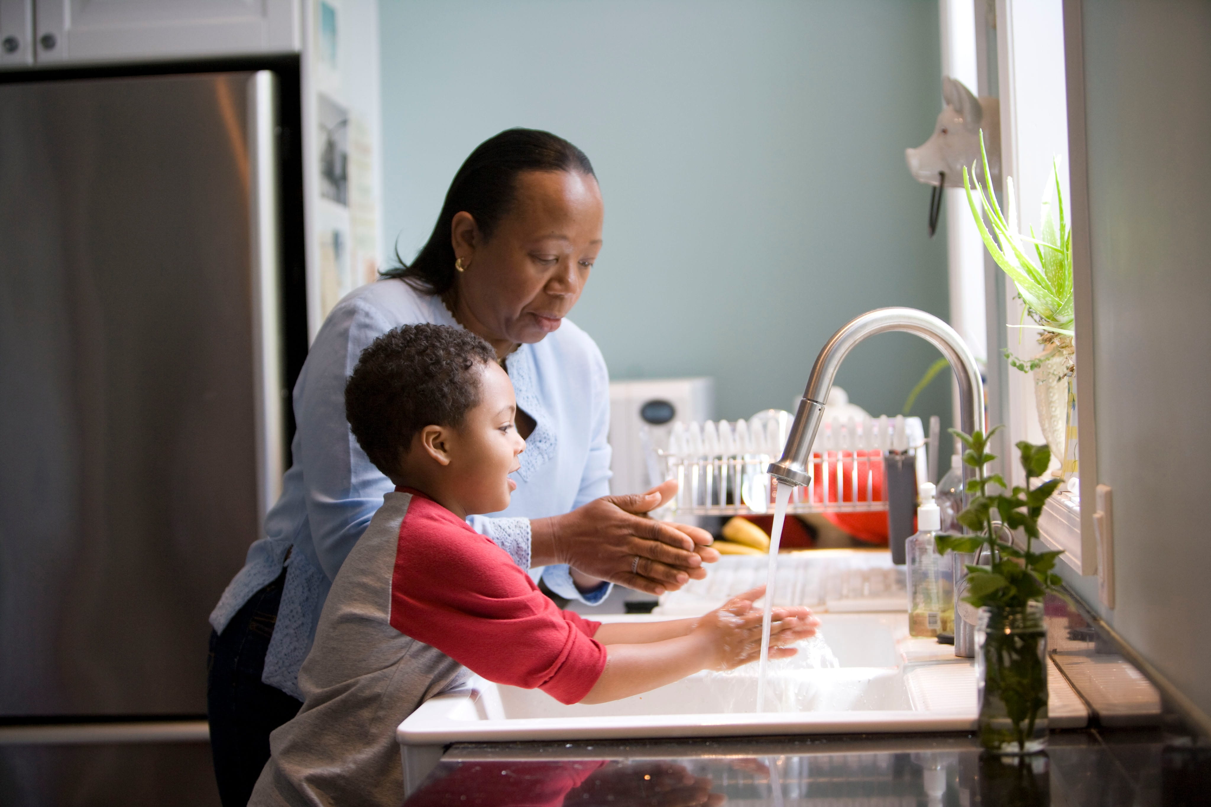 An adult showing a child how to wash their hands at a kitchen sink