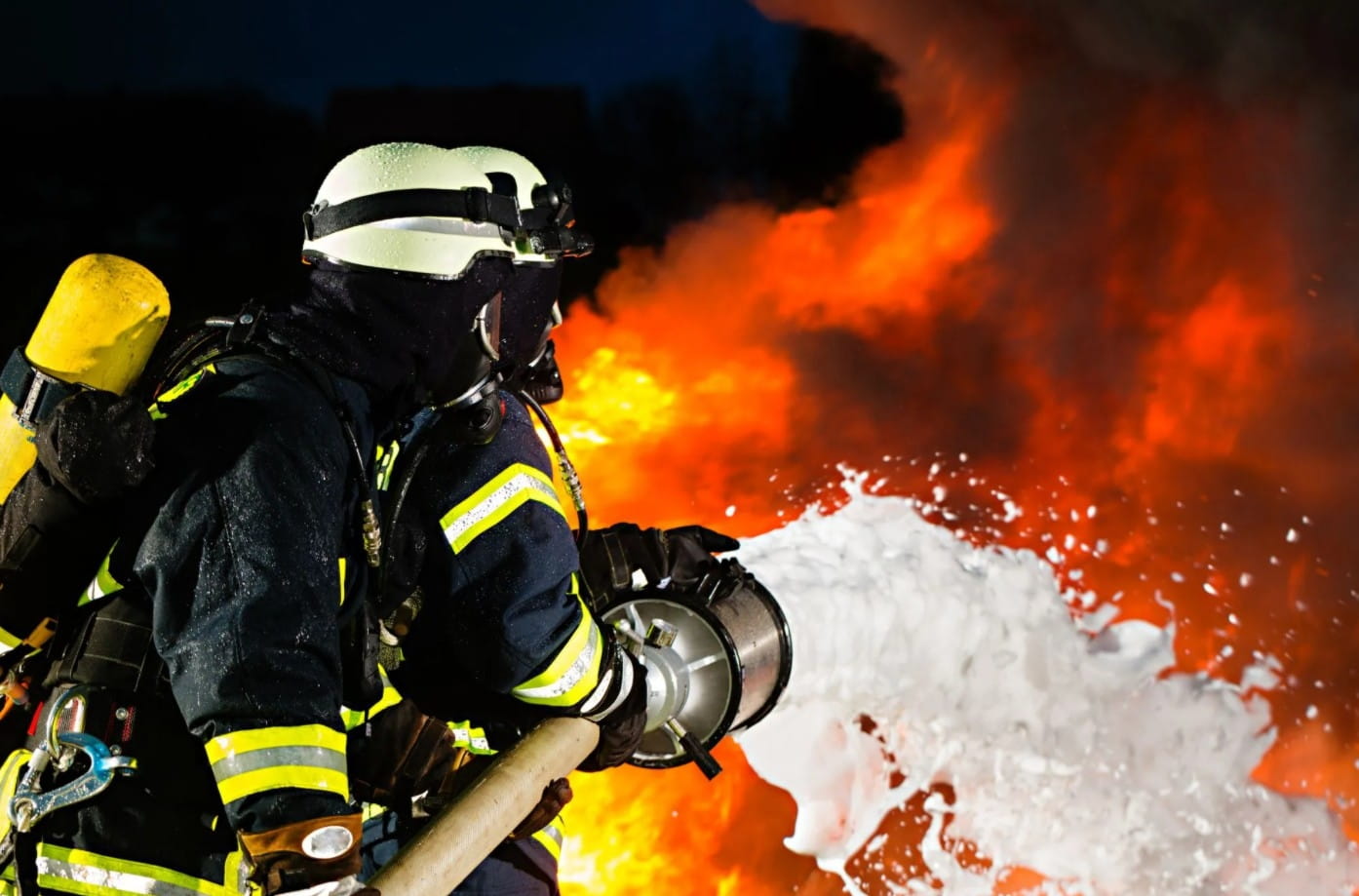 A firefighter spraying bright white foam at a fire