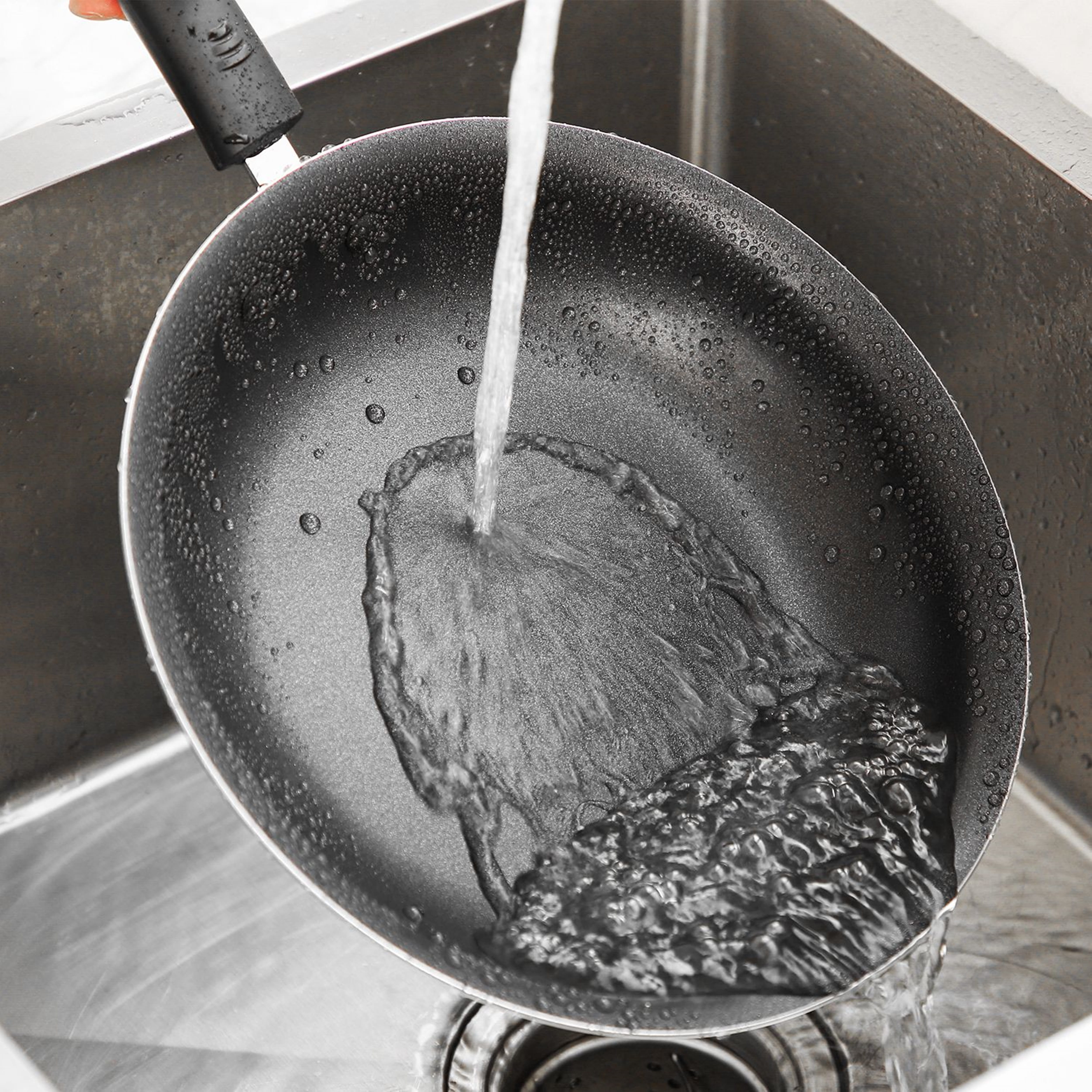 A nonstick frying pan being rinsed in a sink