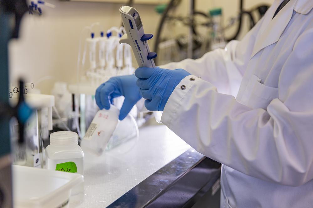A scientist in a lab wearing blue gloves holding a pipette and a test tube