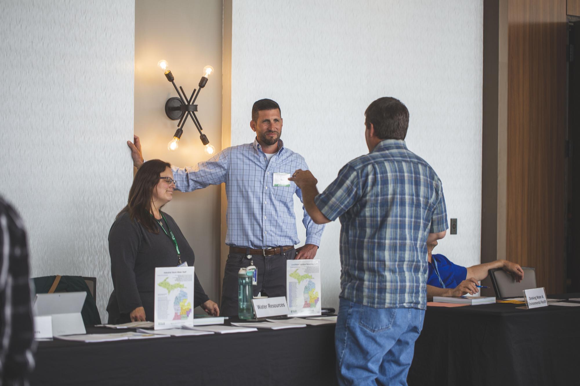 Two EGLE employees from the Water Resources Division talking to a resident at a resource fair; there is a table with handouts and maps between them