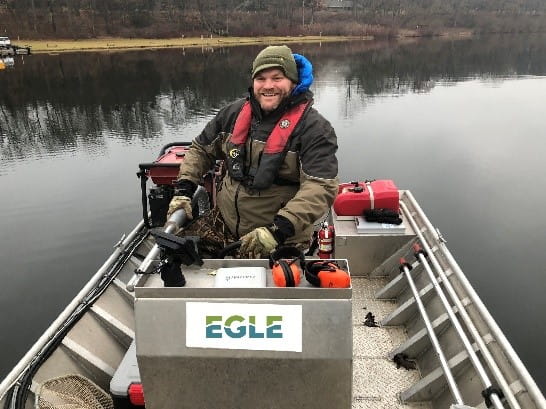 An EGLE staff person sitting on a boat on a lake with sampling equipment