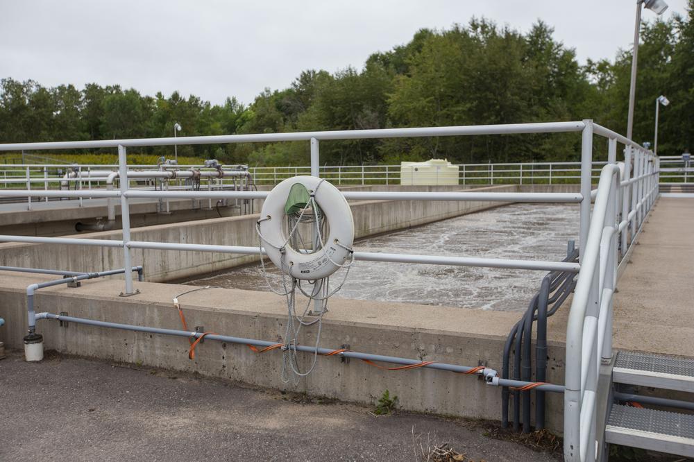 A wastewater treatment plant basin filled with waste water. A life preserver hangs on the fence.