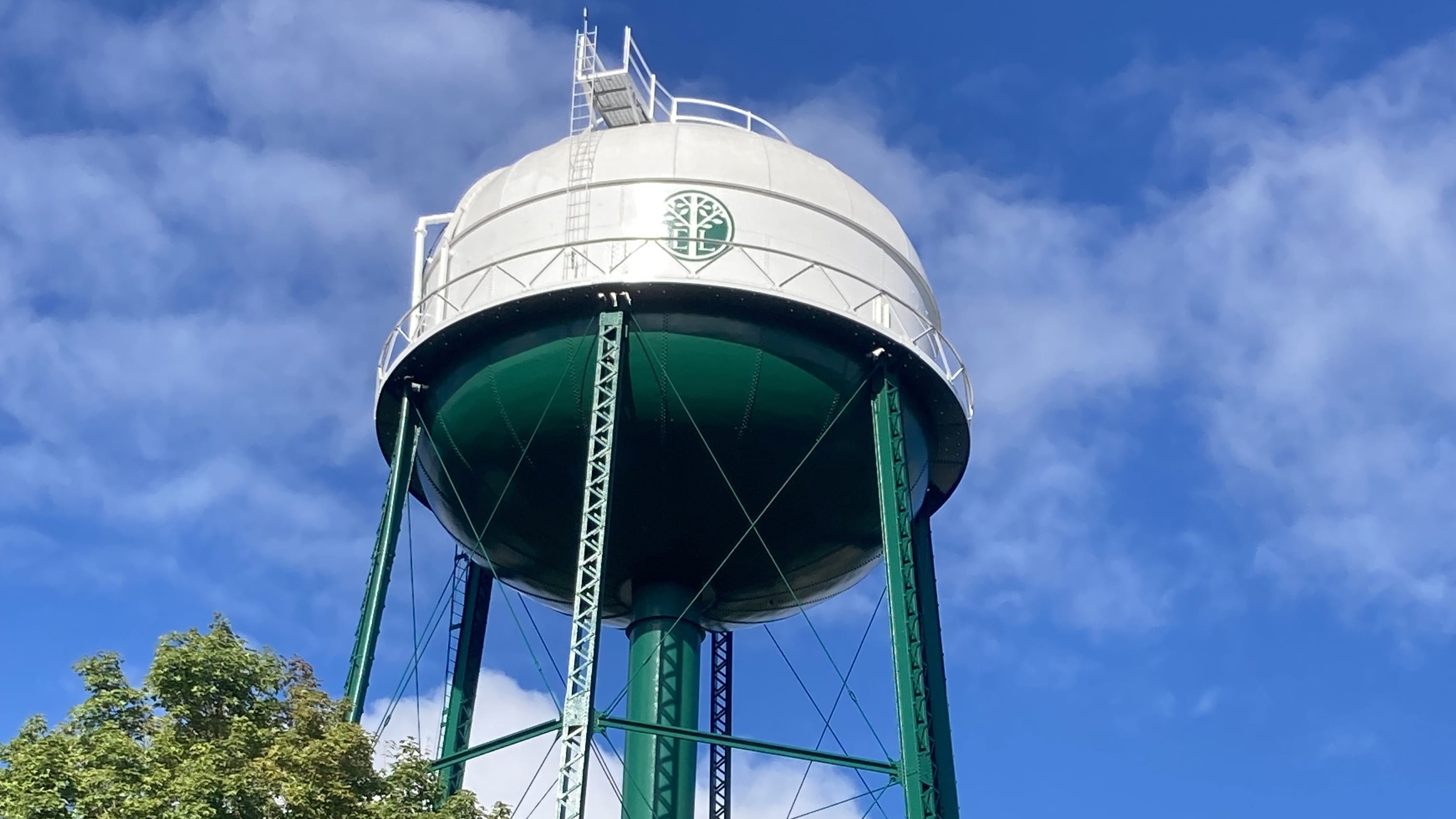 A green and white water tower with "EL" for East Lansing on it, standing tall against a bright blue sky