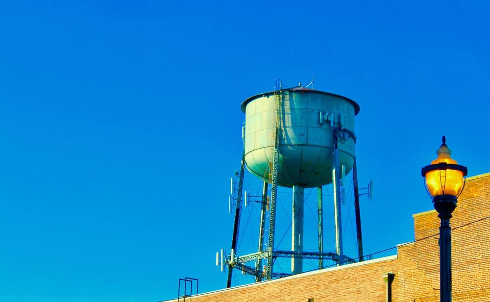 A green water tower stretching up into a blue sky