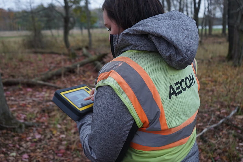 An AECOM contract employee standing at the House Street Disposal Area in Belmont, Kent County, holding a tablet