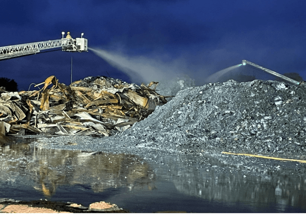 Two firefighters spraying water from the ladder of a firetruck on piles of debris at the Menominee Warehouse