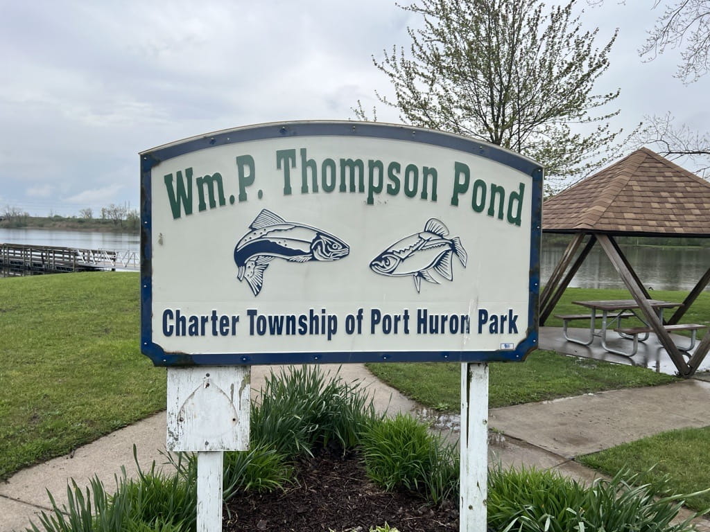 A sign at a park reading William P Thompson park with two fish carved on it