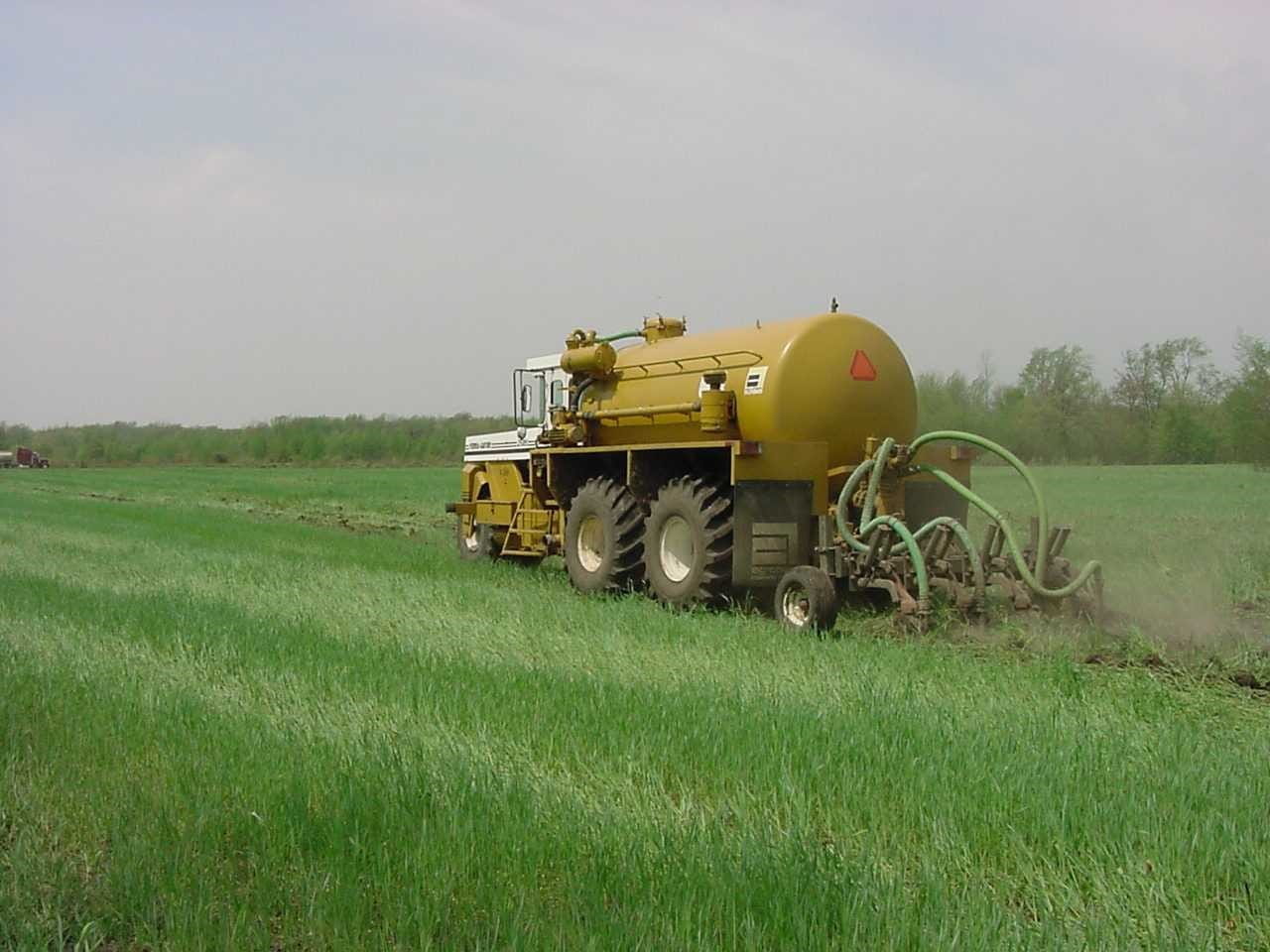 A large yellow tanker driving through a farm field applying biosolids