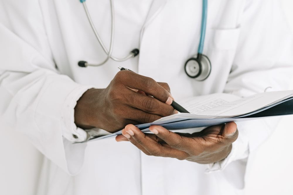 A doctor wearing a white lab coat and a stethoscope, holding a notepad and taking notes