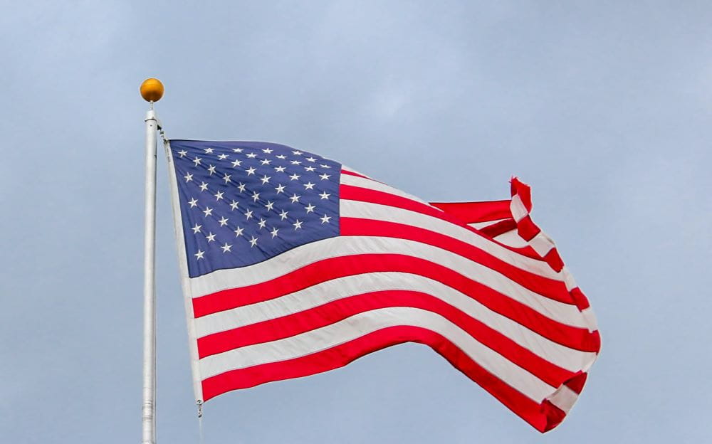 A United States of America flag against a blue sky, blowing in the breeze