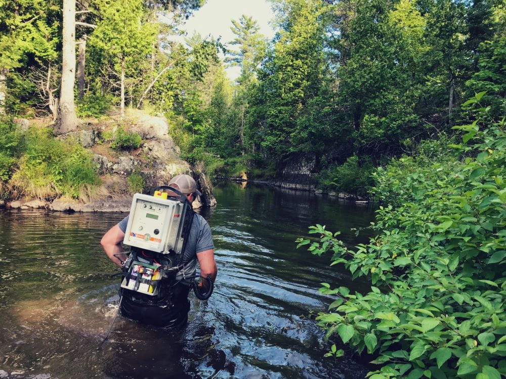 An EGLE staff person waist-deep in a stream with equipment on their back for eFishing
