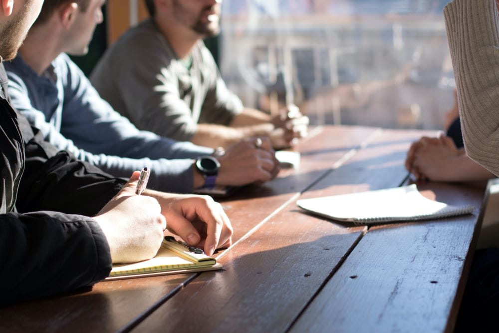 Four people with notepads sitting at a table taking notes