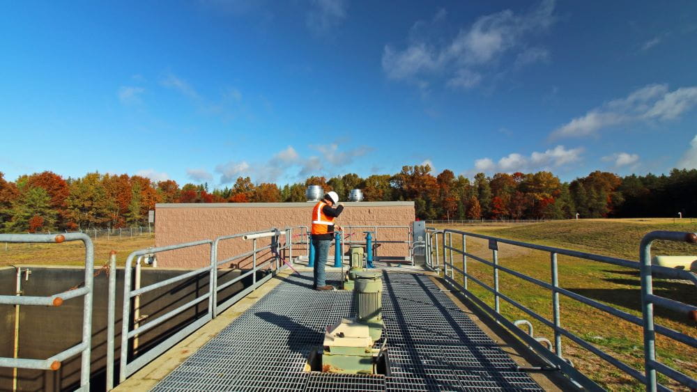 An EGLE staff member standing on a landing at a wastewater treatment plant conducting sampling on a sunny autumn day