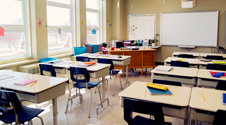 Classroom with several desks facing a whiteboard at the front of the room.