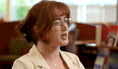 A woman sitting in front of a camera for an interview wearing a cream colored suit jacket