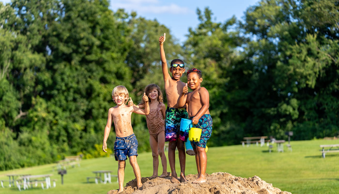 Smiling kids standing on sandy hill with one kids giving thumbs up
