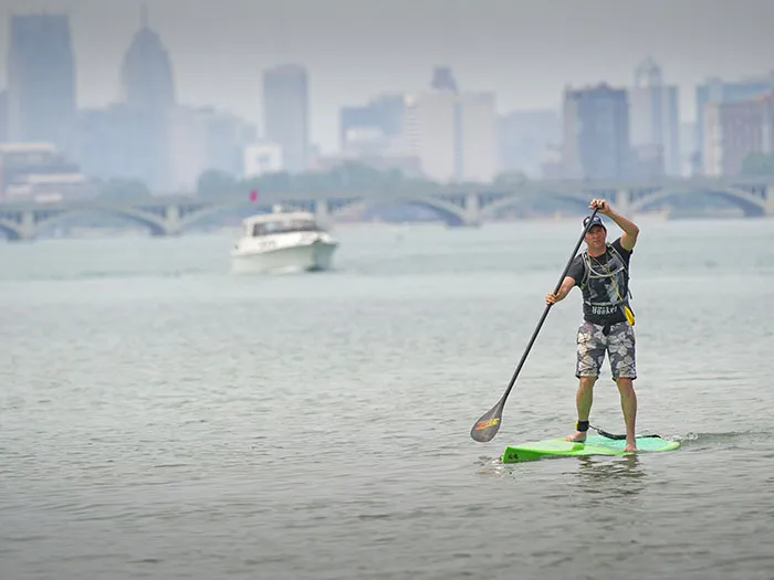 man paddleboarding with skyline and boat in background
