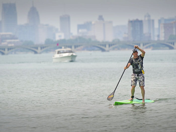 man paddleboarding with skyline and boat in background