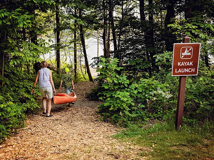 woman and kid walking kayak down trail to water photo by Morgan Aislyn Liskey