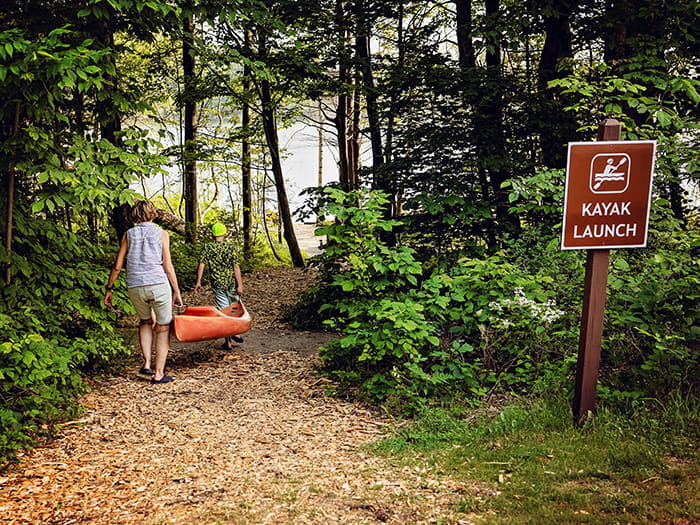 woman and kid walking kayak down trail to water photo by Morgan Aislyn Liskey