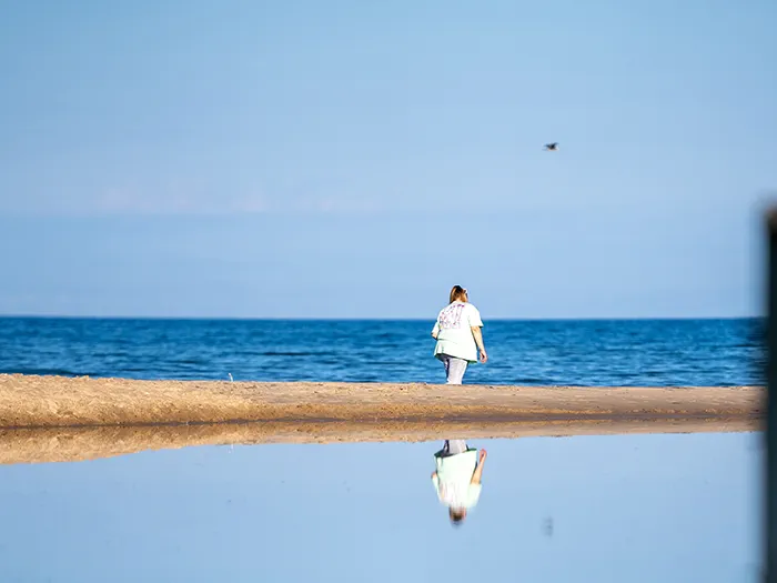 woman walking shoreline with reflection in water